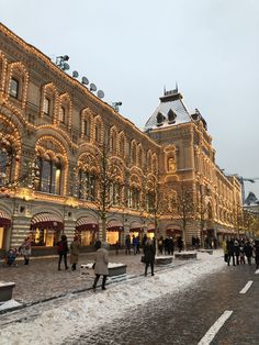 people are walking around in the snow near an old building with christmas lights on it