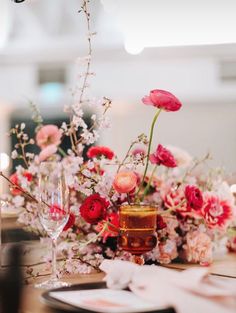 the table is set with pink and red flowers in vases, wine glasses and napkins