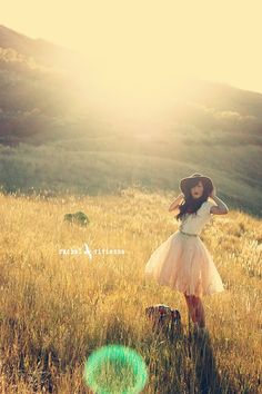 a woman in a dress and hat standing in a field