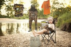 a little boy sitting in a chair next to a lake and some clothes hanging from the line