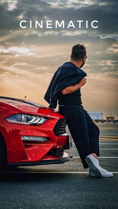 a man sitting on the hood of a red sports car in front of a cloudy sky