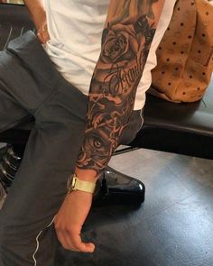 a man with a rose tattoo on his arm sitting in front of a black table