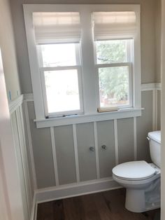 a white toilet sitting next to a window in a bathroom on top of a hard wood floor