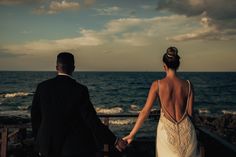 a bride and groom hold hands as they walk towards the ocean