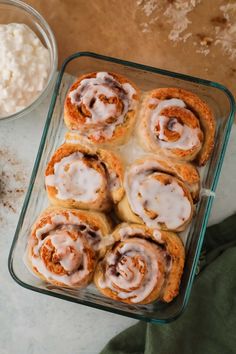 cinnamon rolls with icing in a glass baking dish next to some whipped cream and other ingredients