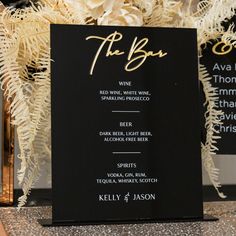 a black and white menu card with gold lettering on it sitting next to a vase filled with flowers