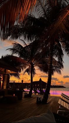 the sun is setting behind some palm trees on a deck overlooking water and boats in the distance