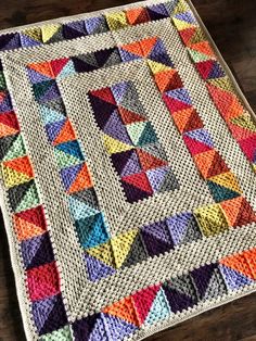 a multicolored quilt on a wooden floor with a table topper in the background