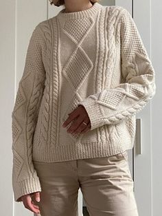 a woman standing in front of a door wearing a white sweater and khaki pants