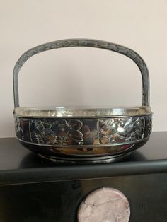 a metal basket sitting on top of a black table next to a penny coin in front of a white wall