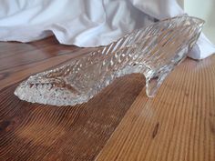 a glass shoe sitting on top of a wooden floor next to a white bed sheet