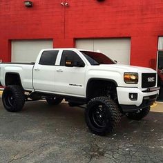 a white truck is parked in front of a red building with black tires and rims