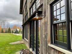 a lamp hanging from the side of a wooden building next to a green field and trees