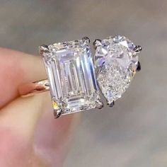 someone is holding an engagement ring that has two emerald cut diamonds on the side and one diamond in the middle