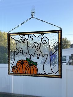 a stained glass window with ghost and pumpkins hanging from it's side in front of a white fence