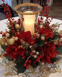 a candle is lit on top of a table with red flowers and greenery in it