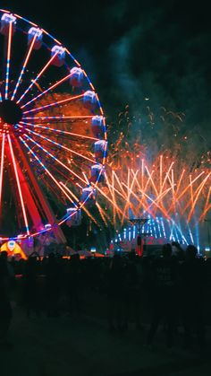 fireworks are lit up in the night sky near a ferris wheel