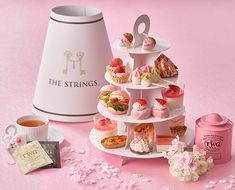 a pink table topped with lots of cupcakes and pastries next to a teapot