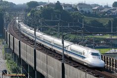 a white train traveling down tracks next to a lush green hillside covered with trees and houses