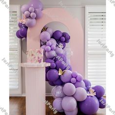 purple balloons are arranged in the shape of an arch with a cake and butterflies on it