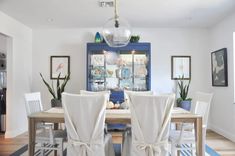 a dining room table with white chairs and a blue china cabinet in the back ground