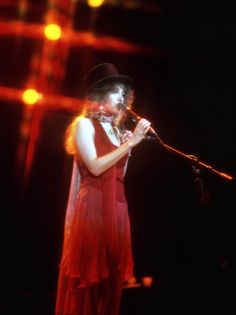 a woman in a red dress and hat singing into a microphone