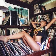 a woman laying on top of a wooden shelf filled with vinyl records and cds in a room