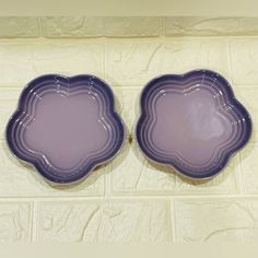 two purple plates sitting next to each other on a tile floor in front of a white wall