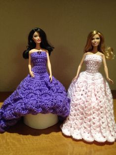 two crocheted barbie dolls in dresses sitting on a table next to each other