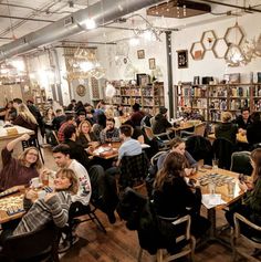 a group of people sitting at tables eating food in a room with bookshelves