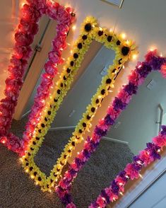 three flower leis in front of a mirror with lights on them and one is pink, yellow and purple