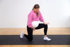 a woman in pink shirt and black leggings doing squat exercises on yoga mat