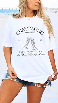 a woman standing on the beach wearing a white t - shirt that says champagne problems