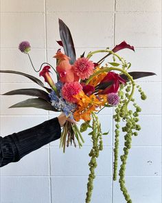 a person holding a bouquet of flowers in front of a white brick wall with green stems