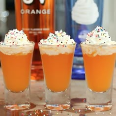 three glasses filled with orange liquid and sprinkles next to a bottle of booze