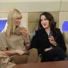 two women sitting on an airplane drinking wine