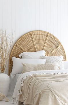 a wicker headboard with white linens and pillows on a bed in a bedroom