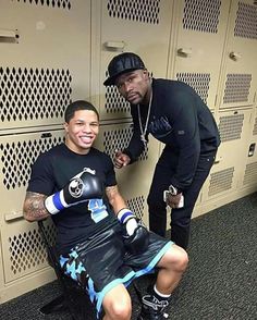 a man sitting in a locker room next to another man wearing boxing gloves and knee pads