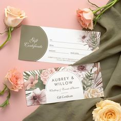 two wedding cards with flowers on them next to green cloth and pink rose bouquets