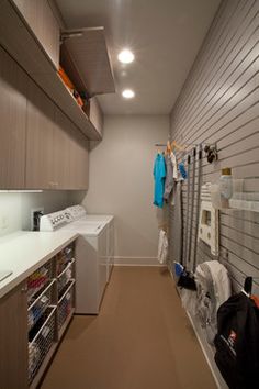 a long narrow laundry room with clothes hanging on the wall and cabinets in the closet