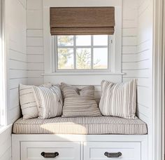 a window seat with pillows on it in the corner of a room that has white shiplap walls