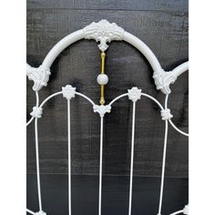 a white iron bed frame with gold and white decorations on the top, against a black background