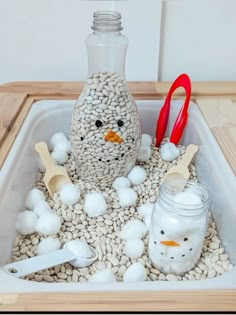 a snowman made out of rocks and plastic spoons sitting in a container filled with cotton balls