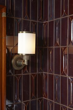 a bathroom light that is on the side of a wall with brown tiles behind it