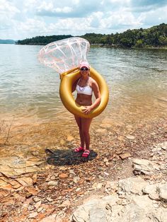 a woman holding an inflatable object while standing on the shore of a lake