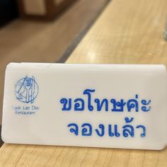 a close up of a white and blue sign on a wooden table with writing in thai