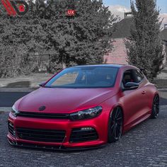 a red car parked in front of some trees