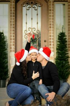 a man and woman kissing while sitting on the ground in front of a house with christmas decorations