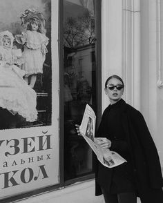 black and white photograph of a woman reading a newspaper in front of a store window