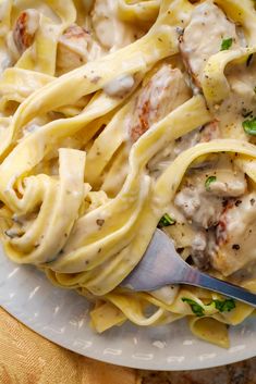 a white plate topped with pasta covered in sauce and chicken meat on top of it